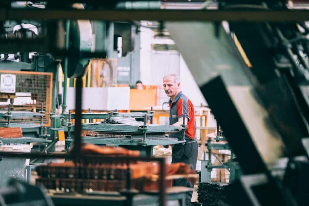 Man in a grey and red shirt operating industrial machinery inside a factory