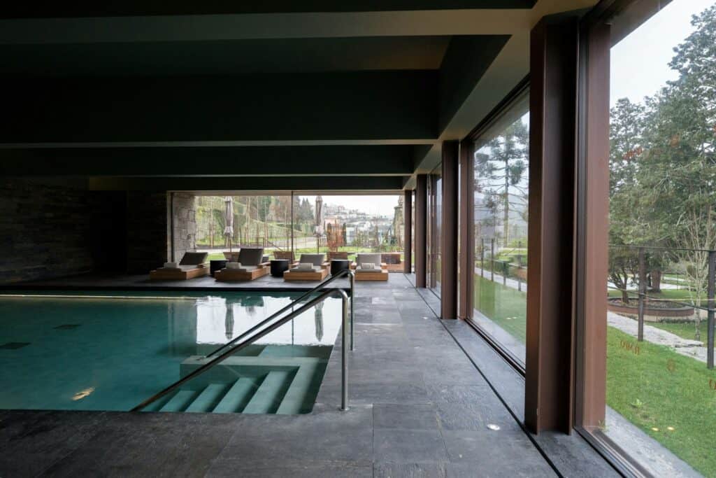 Indoor swimming pool with lounge chairs beside large windows, a relaxing setting for a spa break